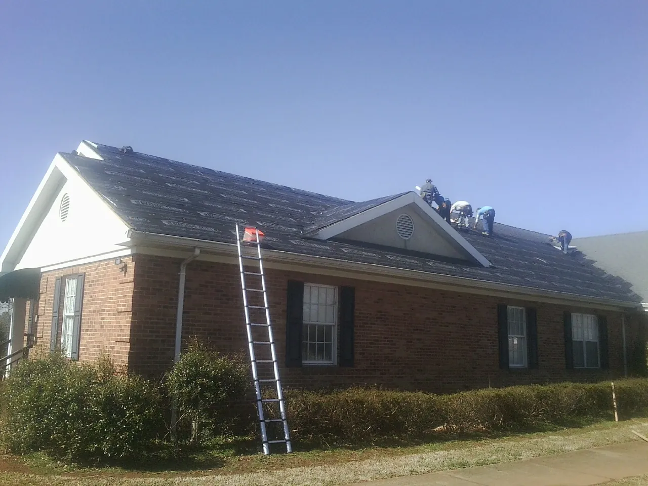 Crew tearing shingles off a brick ranch roof with a ladder set — Metal Roof Repair work by our crew in Brandon