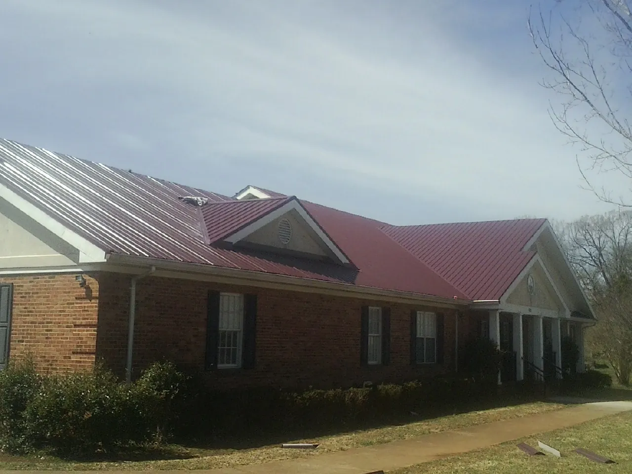Red metal roof with gabled entries on a long brick building, from a Hail Damage Roof Repair job in Brandon